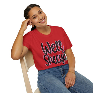 Woman wearing red casual statement tee with "Well Sheeyit!" text sitting on wooden chair