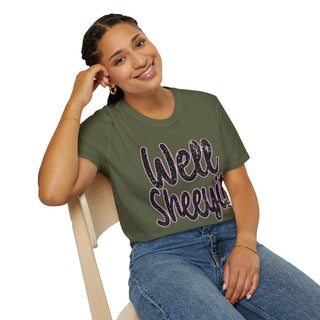 Woman wearing olive green casual statement tee with "Well Sheeyit!" text design sitting on chair