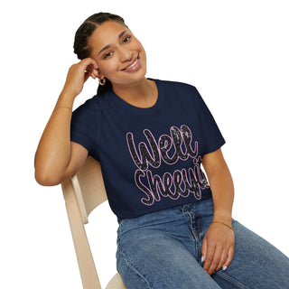 Woman wearing navy blue casual statement tee with "Well Sheeyit!" text sitting on chair