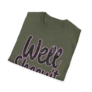 Folded olive green casual statement tee with "Well Sheeyit!" printed in distressed black and pink text