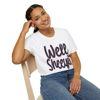 Woman wearing casual white statement tee with "Well Sheeyit!" text sitting on chair