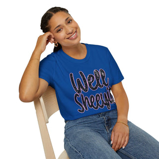 Woman wearing blue casual statement tee with "Well Sheeyit!" text sitting on wooden chair