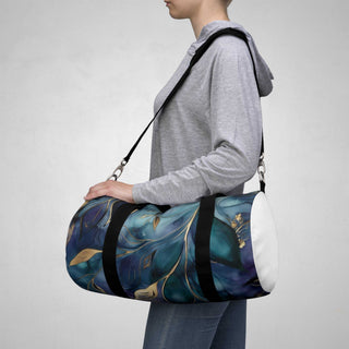 Woman carrying elegant floral duffel bag with blue and gold leaf pattern and black adjustable shoulder strap